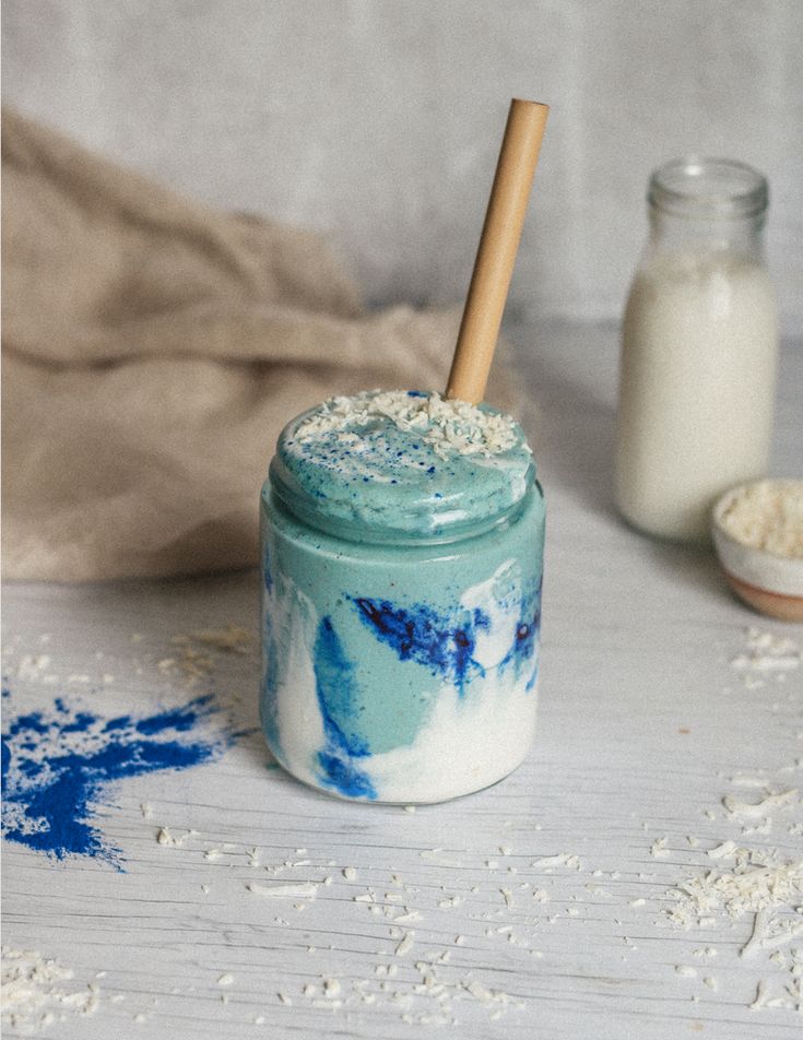Blue and white swirl smoothie with wooden straw, topped with coconut flakes, on a light background.