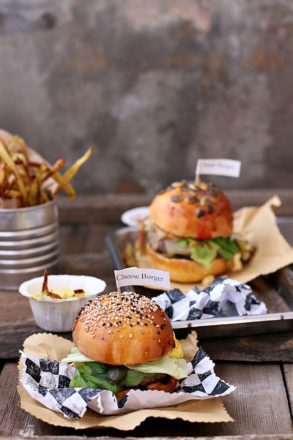 Delicious cheeseburger with sesame seed bun served on rustic tray, accompanied by crispy fries in metal cup.