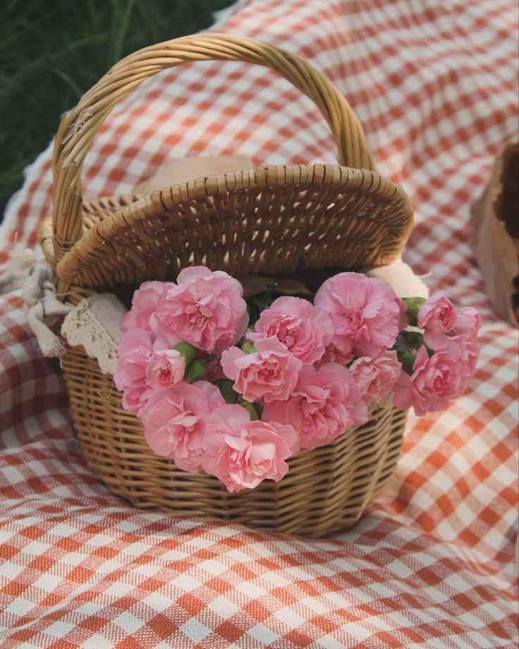 Wicker basket of pink flowers on a gingham picnic blanket, perfect for a spring or summer outdoor setting.