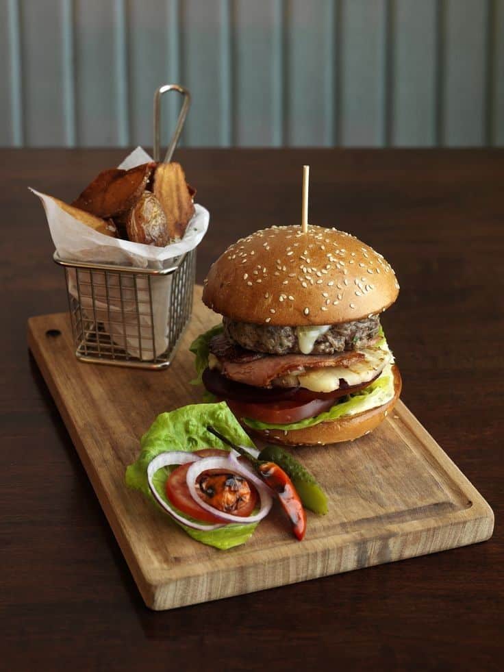 Juicy gourmet burger on wooden board with crispy fries, fresh lettuce, tomato, and onion garnish, perfect for lunch.