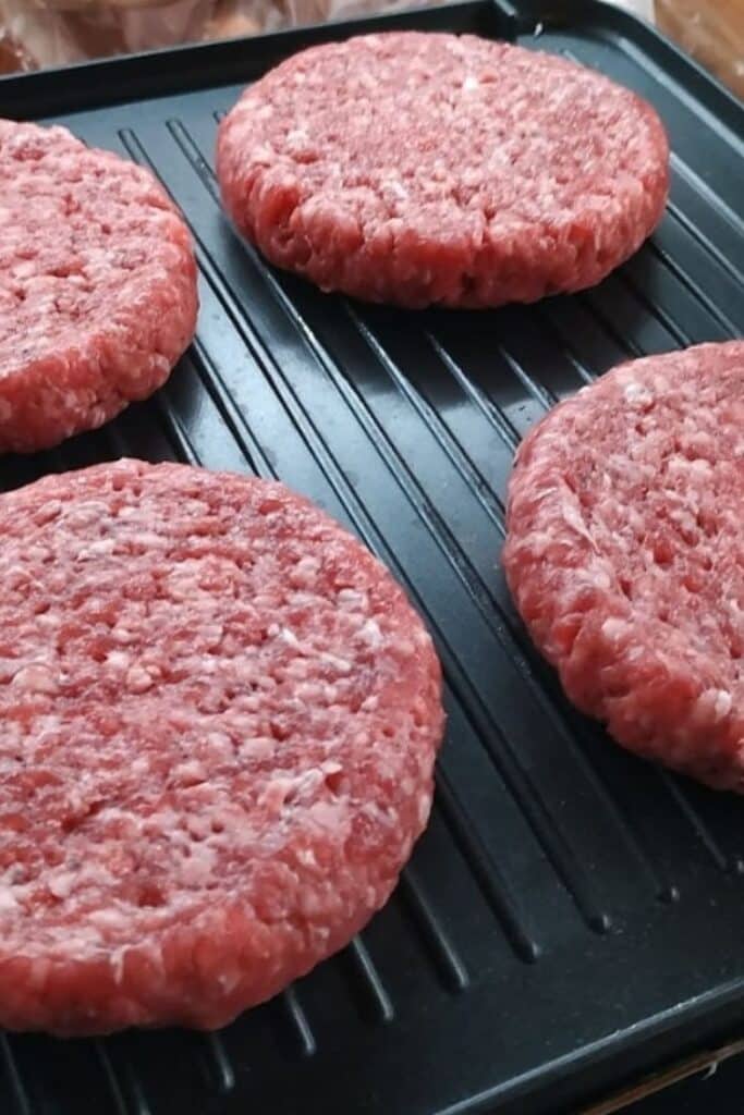 Four uncooked hamburger patties on a grill pan, ready for cooking. Juicy and fresh, perfect for a barbecue.