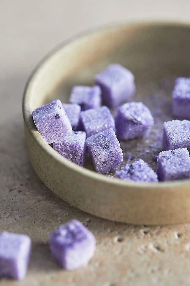 Purple sugar cubes in a beige bowl on a textured surface.