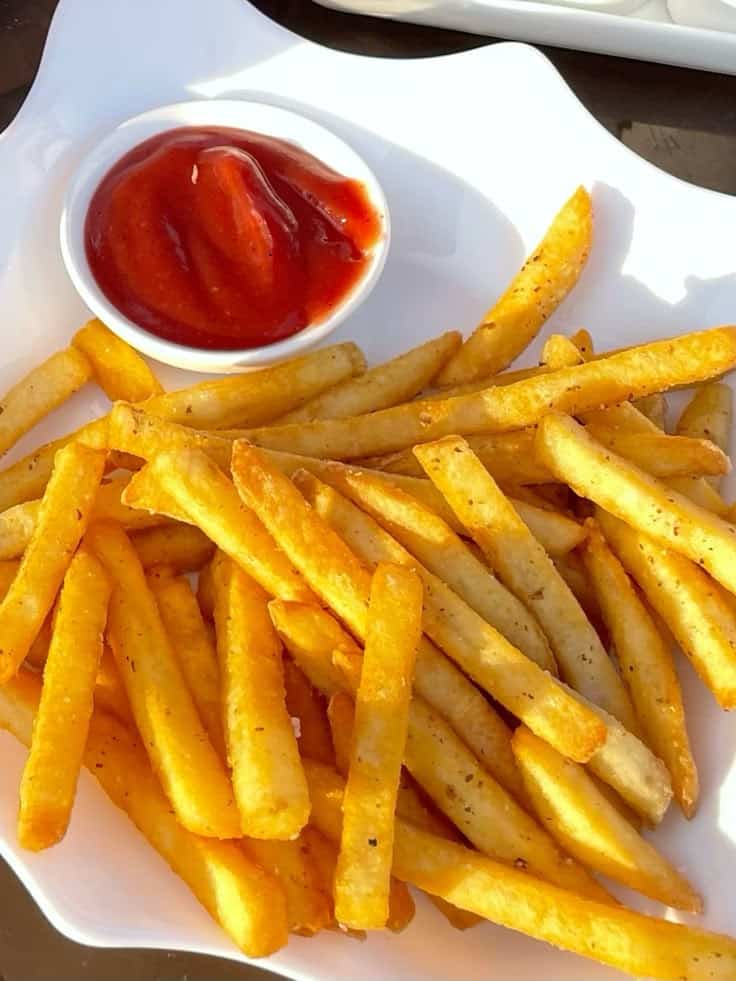 Golden french fries served with a side of ketchup on a white plate.