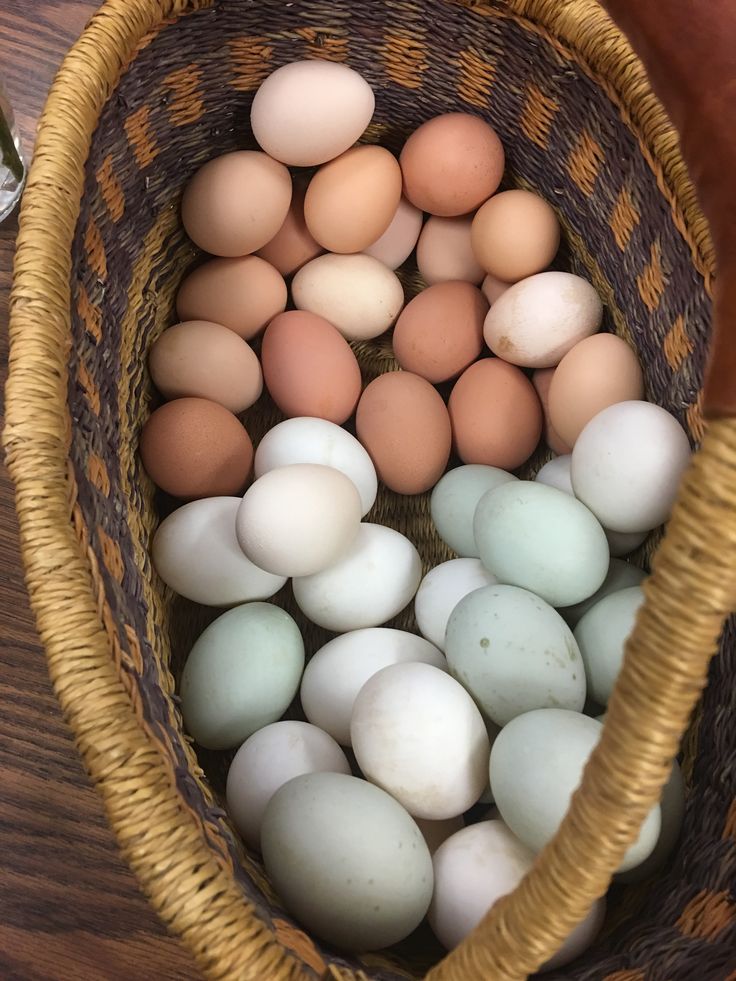 A wicker basket filled with a variety of brown, white, and blue eggs on a wooden surface.