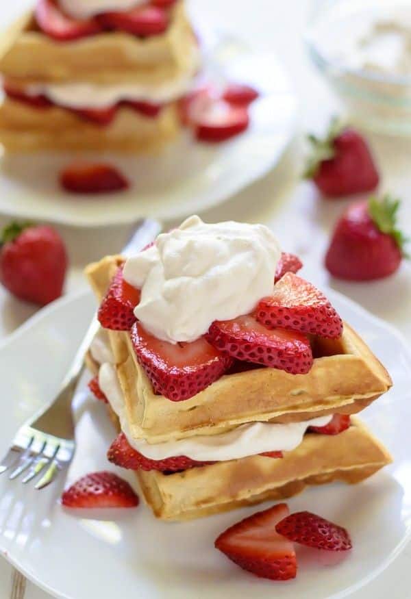 Delicious Belgian waffles topped with fresh strawberries and whipped cream on a white plate, perfect for breakfast.