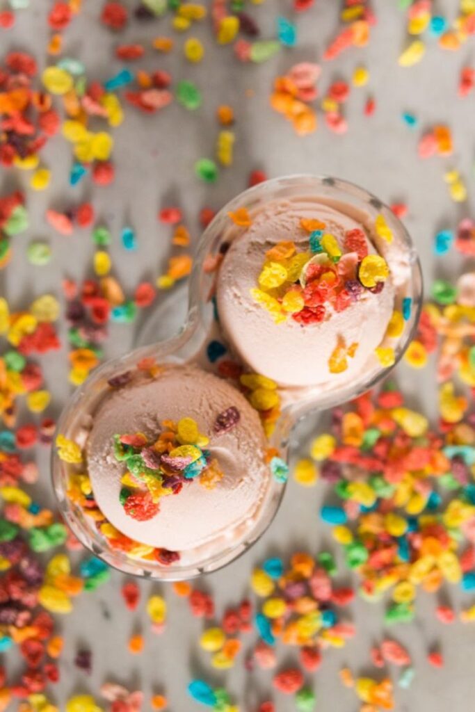 Colorful cereal-topped ice cream in a bowl, surrounded by scattered cereal pieces. Perfect for a sweet, fun treat.
