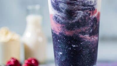 Vibrant purple and pink smoothie in a glass, with milk and berries in the background.