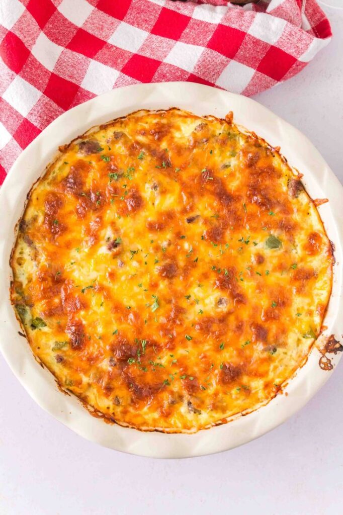Cheesy baked quiche on a red-checkered cloth, topped with herbs for a delicious homemade breakfast.