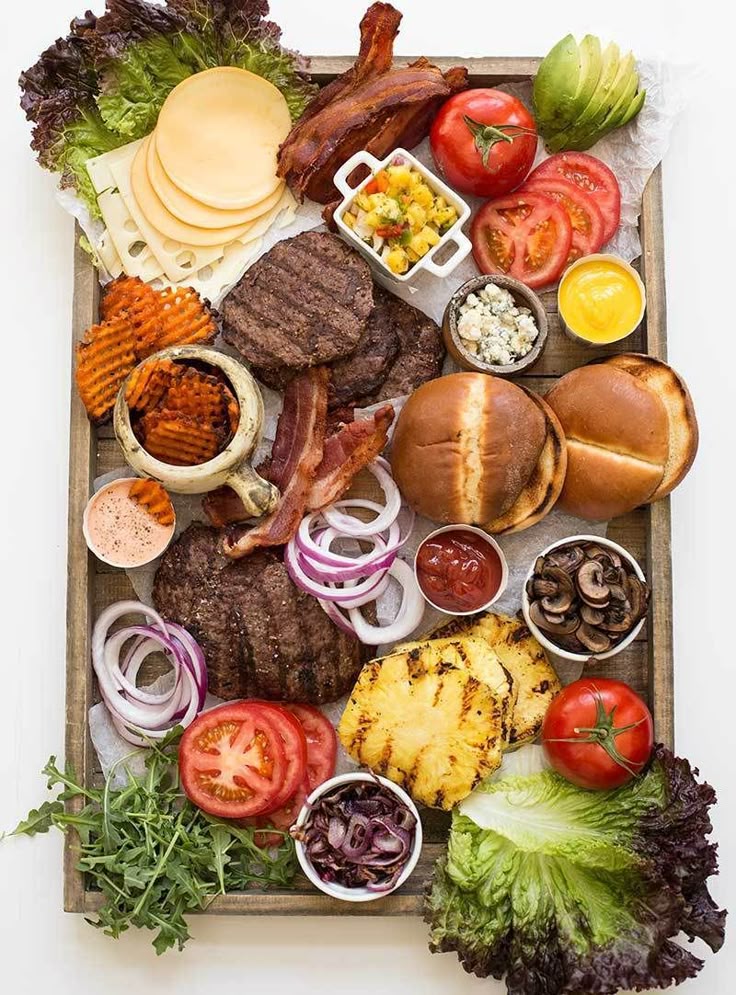 Burger toppings platter with bacon, cheese, buns, vegetables, and sauces, perfect for a customizable meal.