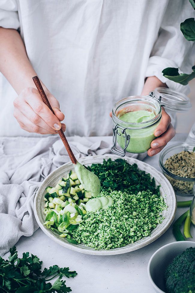 Person preparing a healthy green salad with fresh vegetables and creamy green dressing in a kitchen setting.