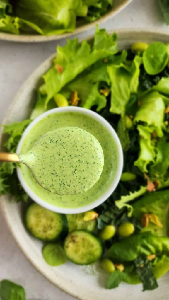 Creamy green salad dressing in a bowl with fresh lettuce, cucumber, and edamame on a plate. Perfect for a healthy meal.