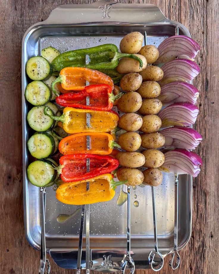 Colorful vegetable skewers with bell peppers, zucchini, potatoes, and onions on a metal tray for grilling.