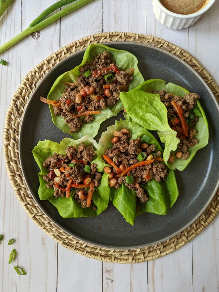 Lettuce wraps with minced beef, carrots, peanuts, and scallions on a plate, served with dipping sauce on the side.