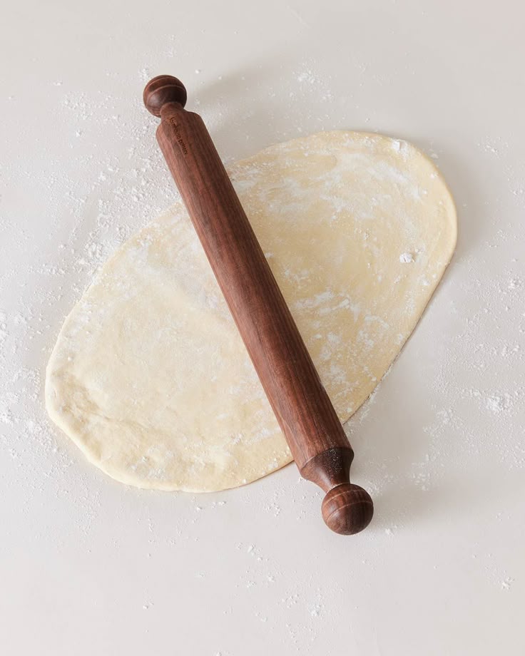 Wooden rolling pin flattening dough on a floured surface for baking or cooking preparation.