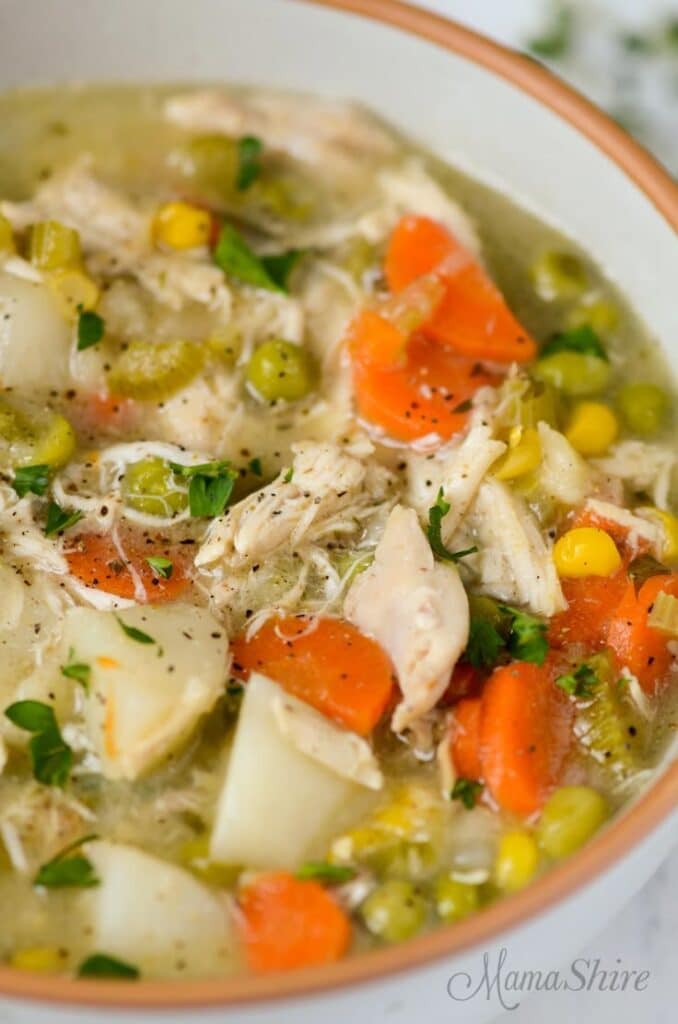 Hearty chicken vegetable soup with carrots, peas, corn, and potatoes in a bowl, garnished with herbs.