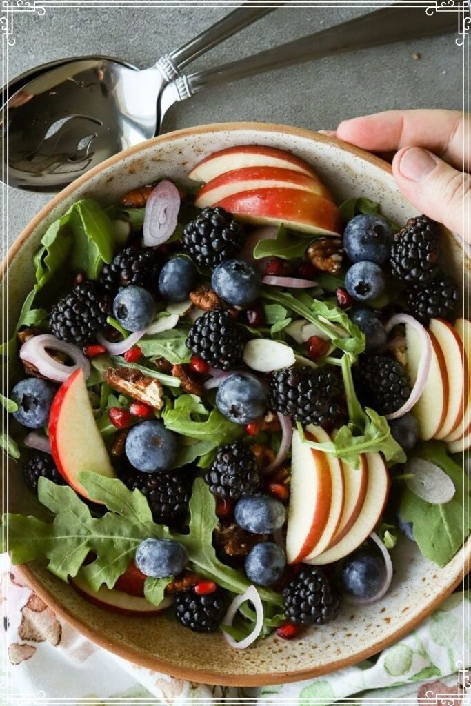 Healthy fruit and greens salad with blackberries, blueberries, sliced apples, and mixed greens in a ceramic bowl.