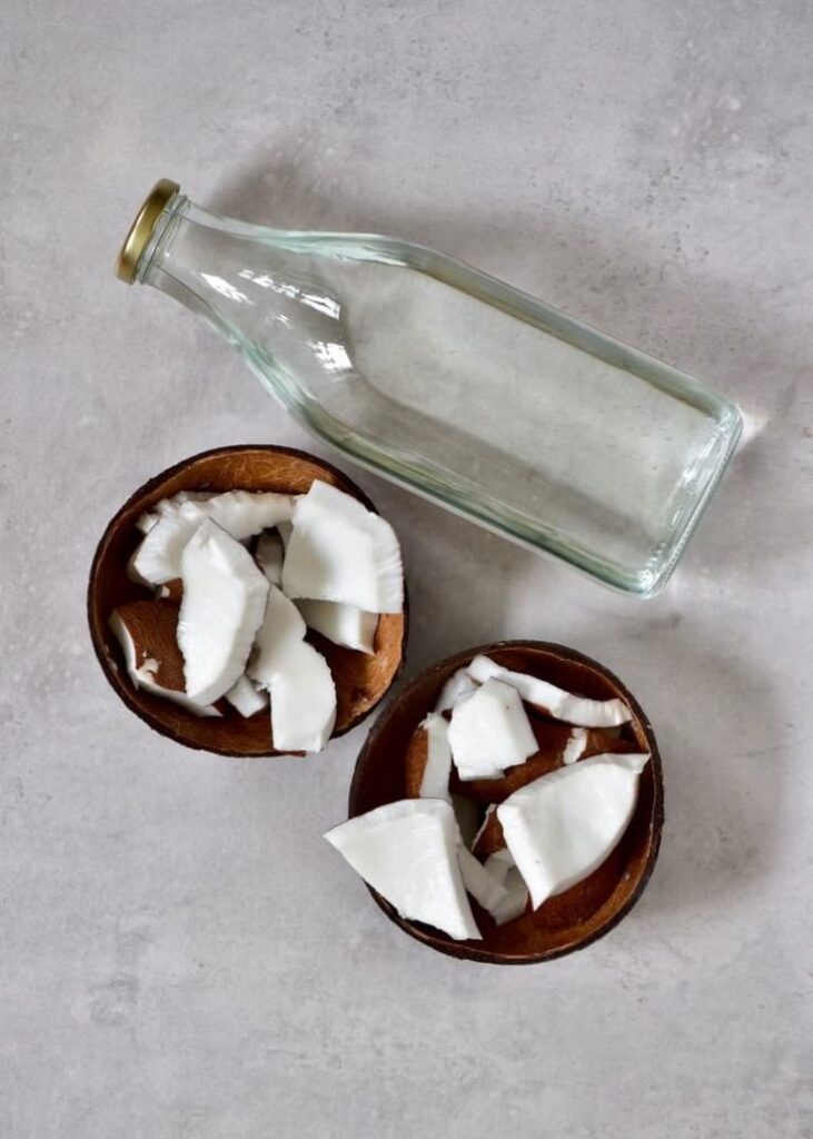 Glass bottle and coconut pieces in bowls on a gray surface.