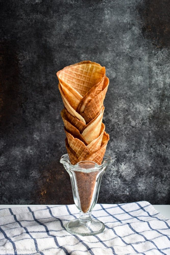 Stack of waffle cones in a glass dish on a checkered cloth, with a dark textured background.