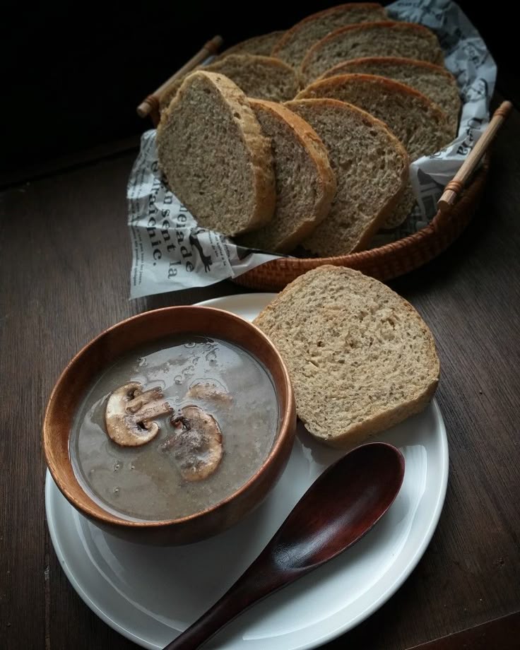 Creamy mushroom soup with sliced bread on wooden table.
