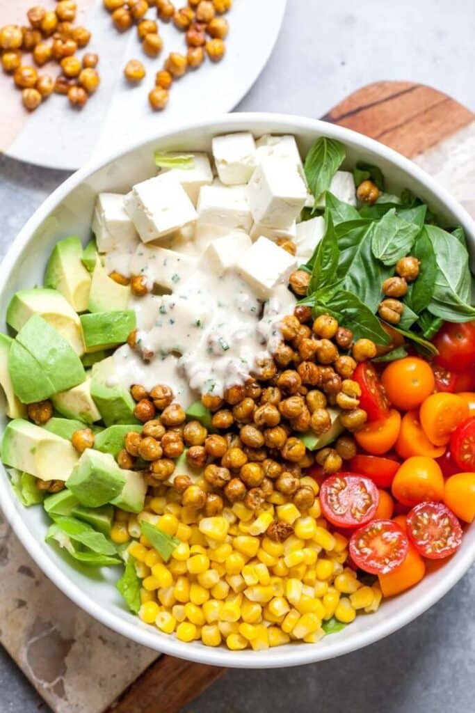 Vibrant salad bowl with avocado, chickpeas, tomatoes, corn, tofu, and creamy dressing, perfect for a healthy meal.