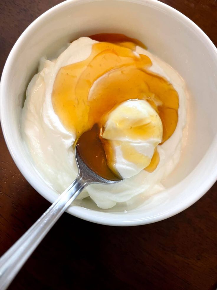 Bowl of creamy yogurt topped with golden honey and a spoon, on a wooden table.