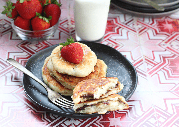Stack of pancakes with strawberries and a glass of milk on a festive table setting.