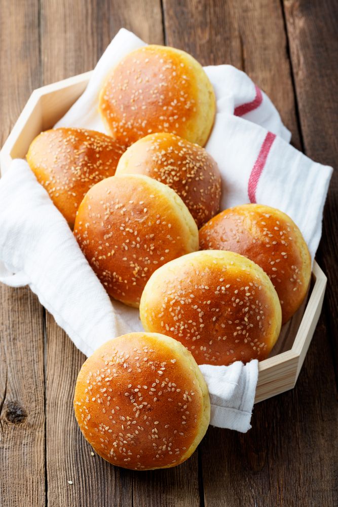 Fresh sesame seed hamburger buns in a wooden basket on a rustic wooden table.