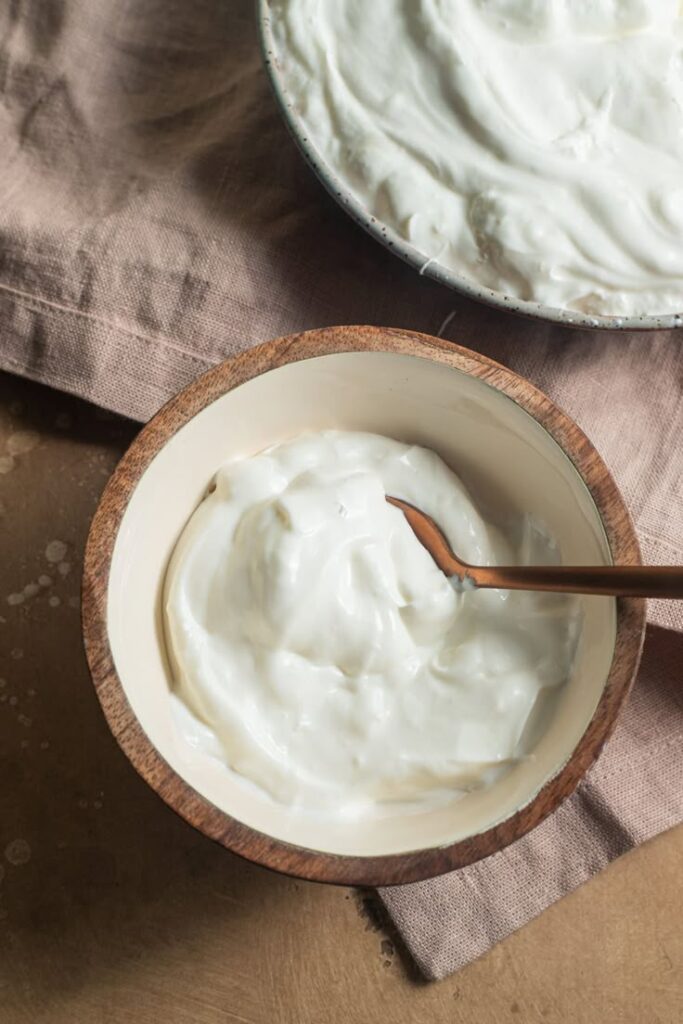 Creamy yogurt in a wooden bowl with a spoon on a rustic cloth background, perfect for healthy eating scenes.