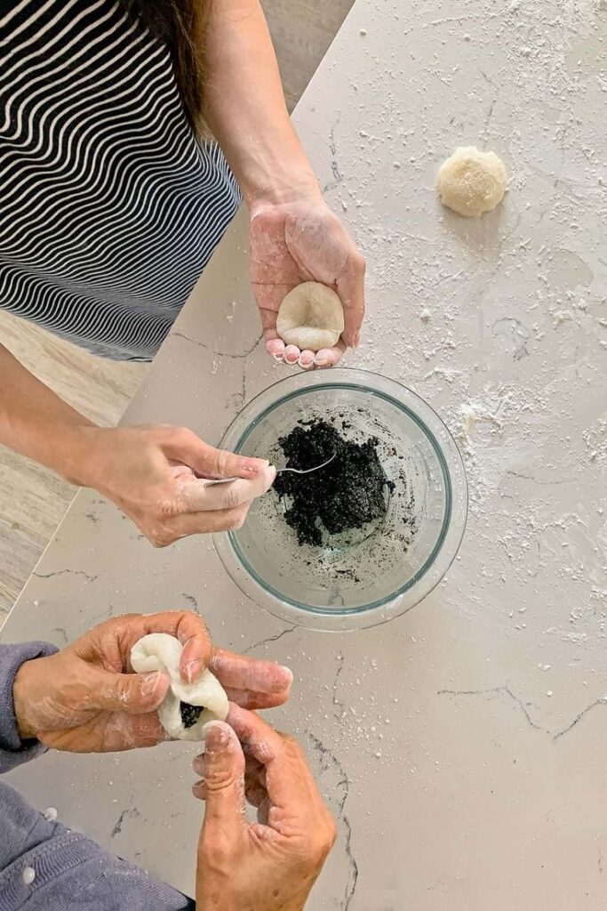 Hands making dumplings with black sesame filling in a kitchen. Flat lay baking scene.