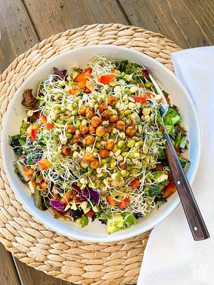 Vibrant salad with chickpeas, sprouts, and mixed greens served in a white bowl on a woven placemat. Healthy meal option.