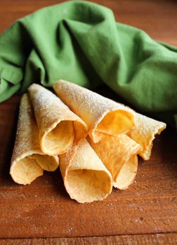 Crunchy rolled wafer cookies on a wooden table with a green cloth background.