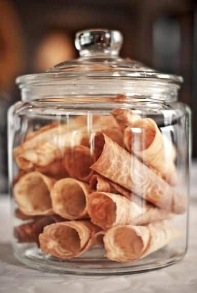 Glass jar filled with rolled wafer cookies on a table, perfect for a dessert display or festive treat.