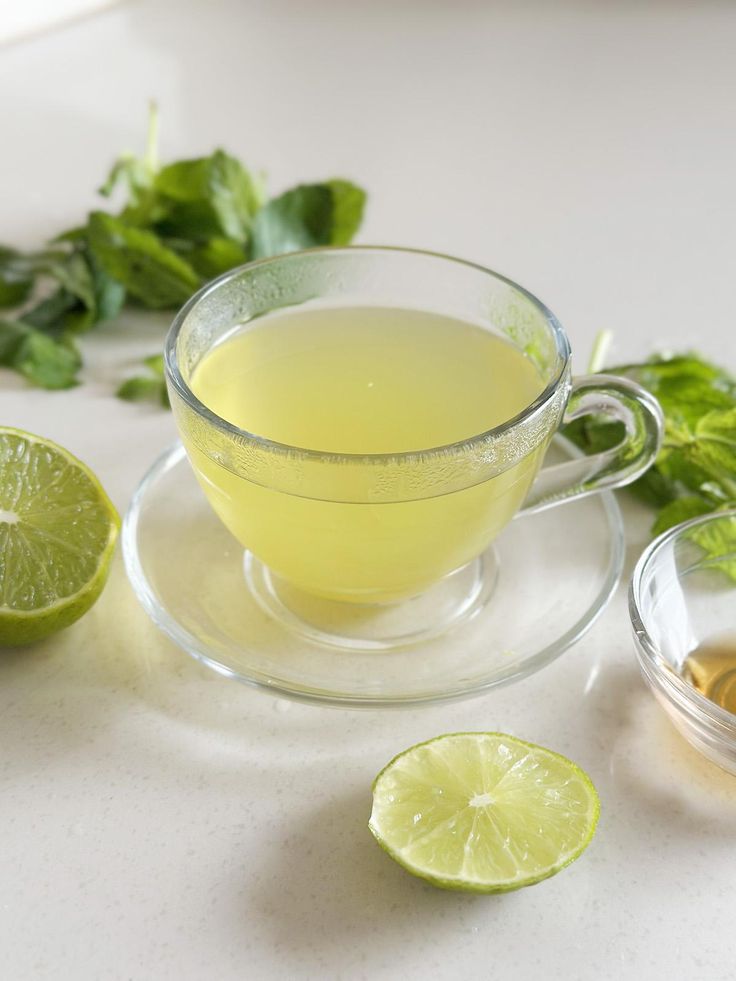 Glass cup of refreshing mint lime tea on a table with fresh lime and mint leaves.