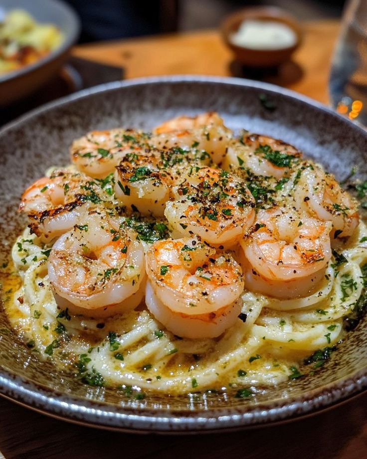 Creamy shrimp Alfredo pasta garnished with herbs, served in a brown bowl on a wooden table.