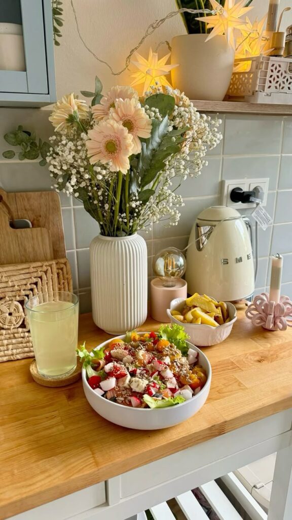 A cozy kitchen scene with a fresh salad, lemonade, and flowers on a wooden countertop.