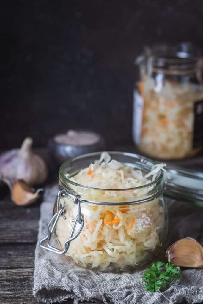 Jar of homemade sauerkraut with garlic and parsley on rustic cloth.