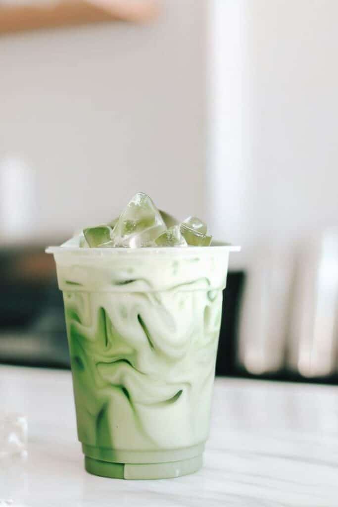 Iced matcha latte in a clear cup on a marble counter, refreshing and creamy green tea drink.