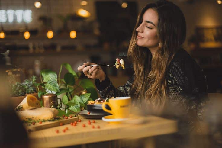 Woman enjoying a meal in a cozy cafe, surrounded by plants and warm lighting.