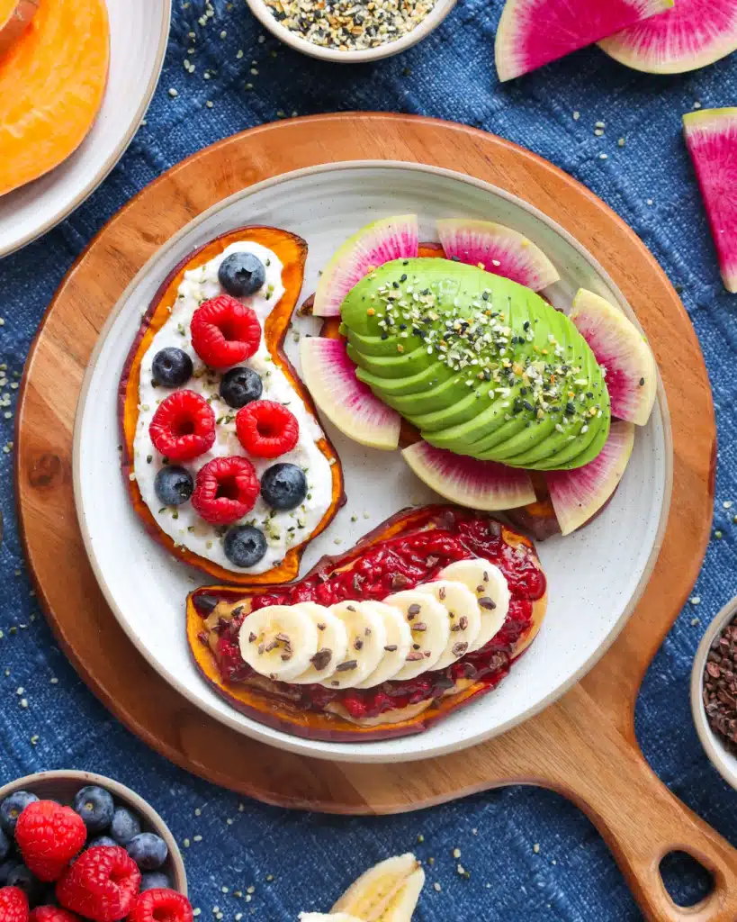 Colorful toast with avocado, watermelon radish, berries, banana, and seeds on a wooden platter.