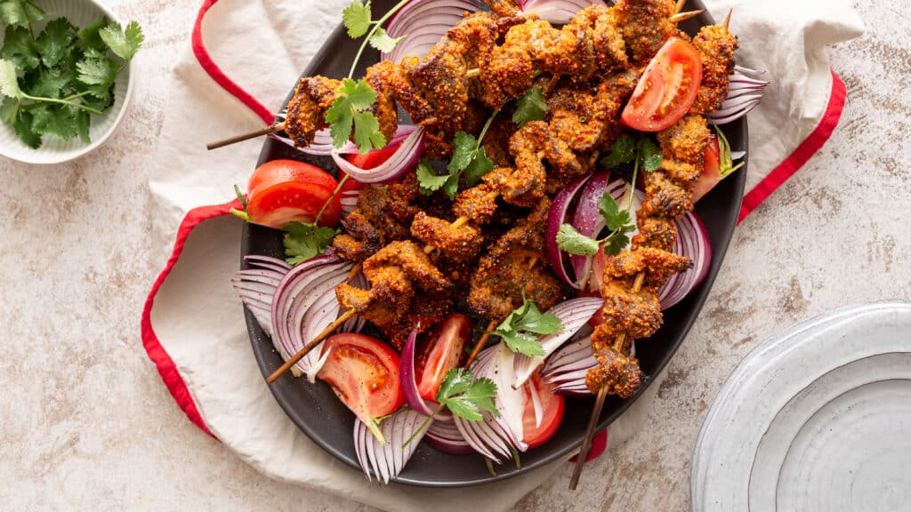 Delicious spicy skewers with tomatoes and onions on a platter, garnished with fresh cilantro.