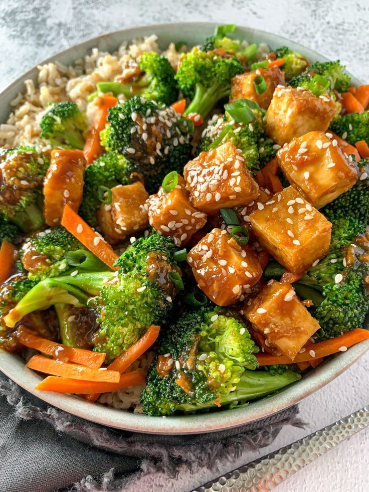Tofu stir-fry with broccoli, carrots, and sesame seeds over brown rice in a bowl. Healthy vegan meal.