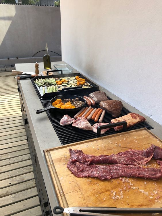 Outdoor barbecue with assorted meats, vegetables, and sausages grilling on a patio.