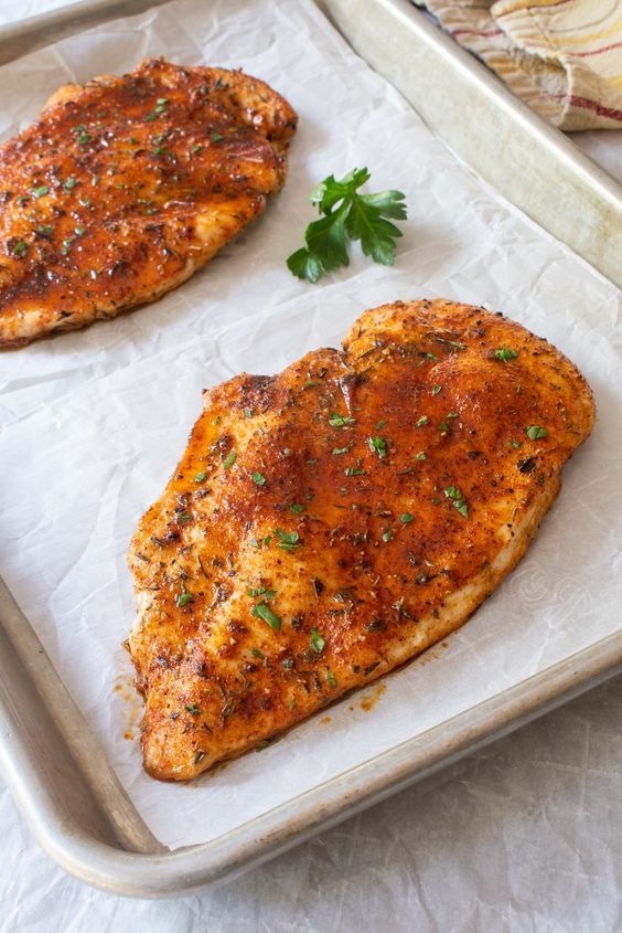Grilled, seasoned chicken breasts on a baking sheet garnished with parsley, ready to serve.