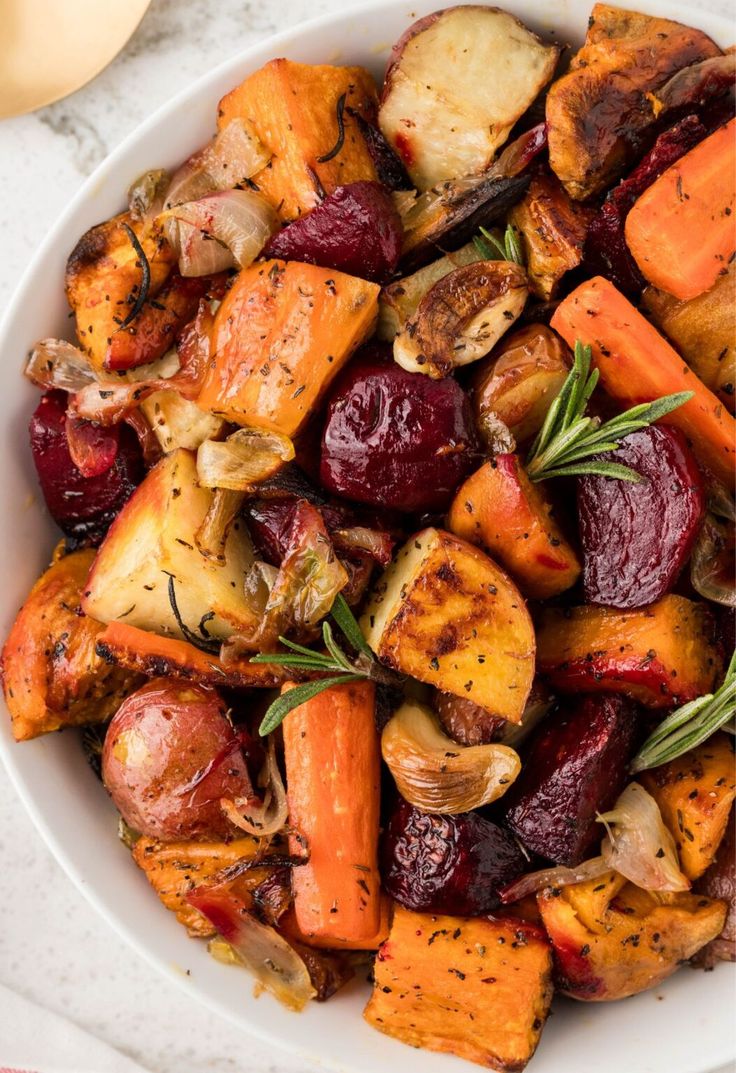 A bowl of colorful roasted root vegetables with herbs, featuring carrots, beets, and sweet potatoes.