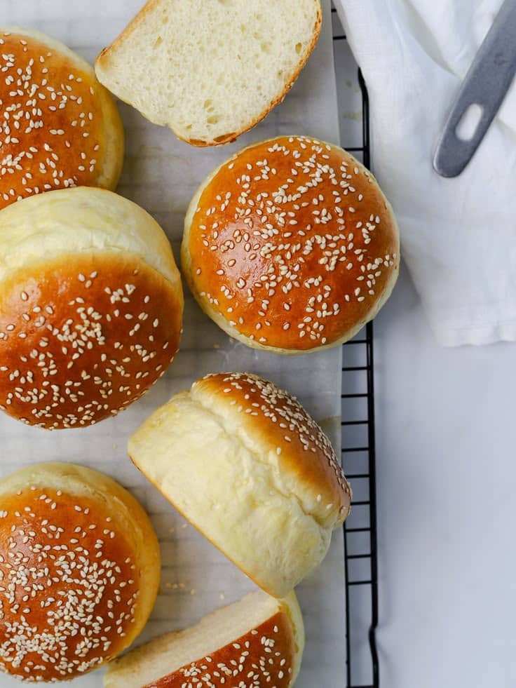 Freshly baked sesame seed hamburger buns on a cooling rack, perfect for sandwiches and burgers.