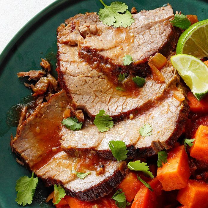Sliced roast beef with cilantro and lime on a green plate, served with sweet potatoes.