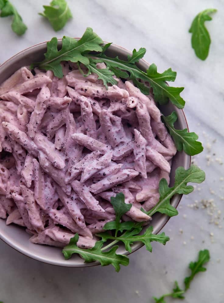 Creamy purple pasta with black pepper and fresh arugula in a bowl on a marble surface.