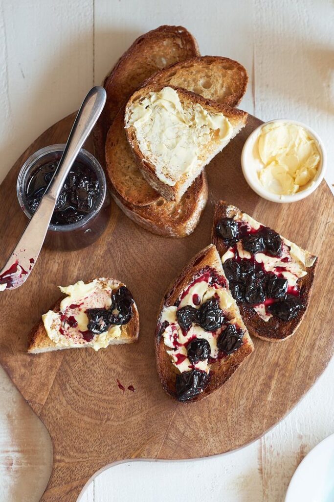 Toasted bread with butter and cherry preserves on a wooden board, perfect breakfast or snack option.