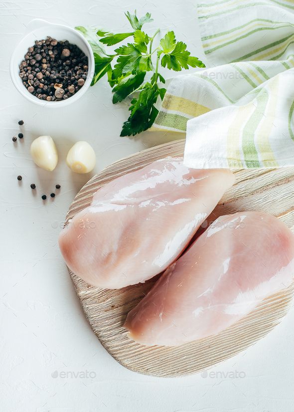 Raw chicken breasts on a wooden board with garlic, peppercorns, and parsley, prepared for cooking.