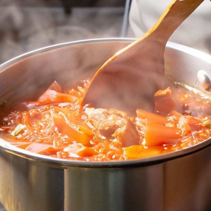 Steaming pot of homemade vegetable soup being stirred with a wooden spoon.